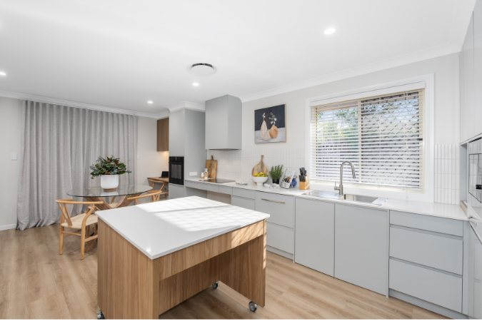 Light grey kitchen with a timber island on castors, dining table and grey curtains beyond — 8 Bishop