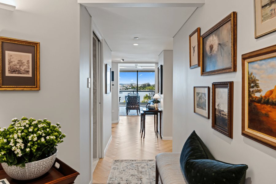 Gallery hallway with framed artwork and a console table, river view through the window beyond — Kangaroo Point / Tess