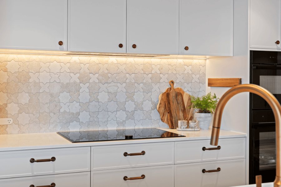 Kitchen splashback in star-and-cross mosaic tile behind the cooktop, brass tapware and timber board — Kangaroo Point / Tess