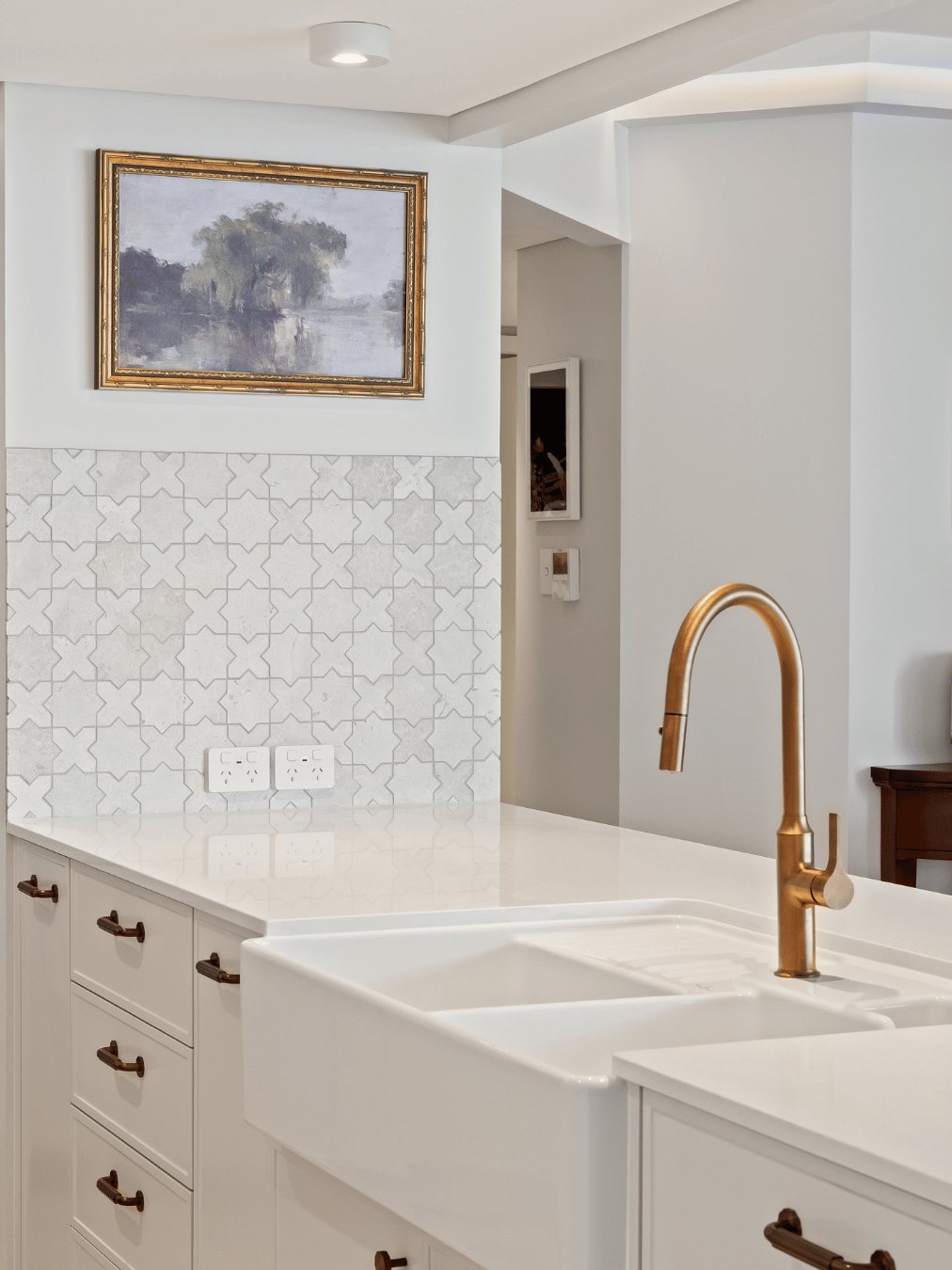 Farmhouse sink and brass tap below a gold-framed landscape painting and mosaic tile splashback — Kangaroo Point / Tess