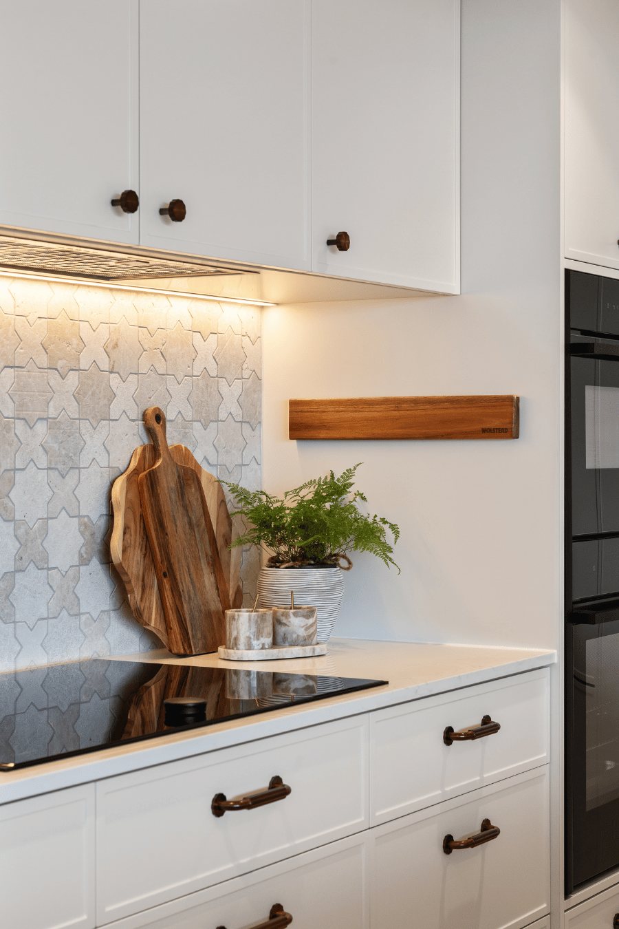Kitchen wall detail with mosaic tile splashback, timber chopping boards and a potted fern — Kangaroo Point / Tess