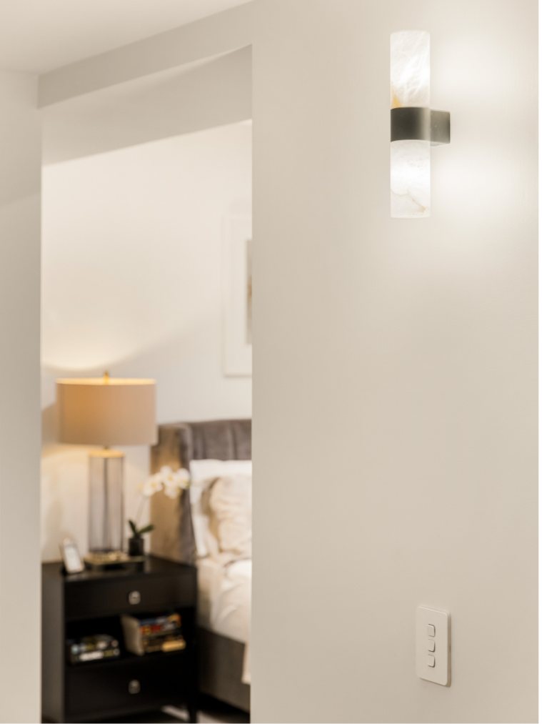 Hallway with an alabaster wall sconce, bedroom glimpsed through the doorway beyond — Kangaroo Point Villa 8