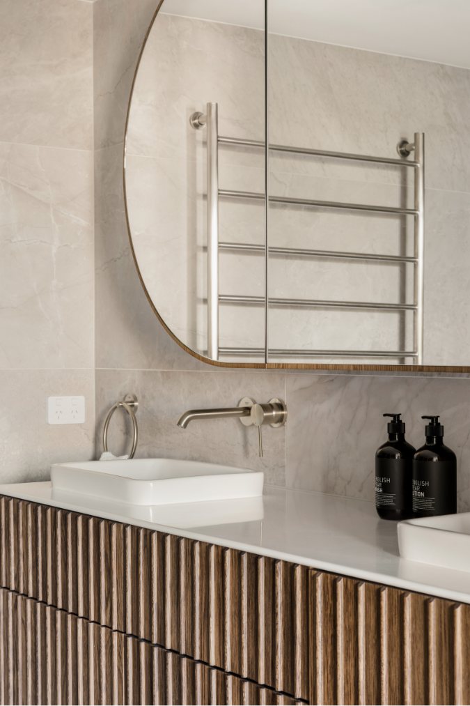 Bathroom vanity detail with a round mirror, heated towel rail and brass tapware — Kangaroo Point Villa 8