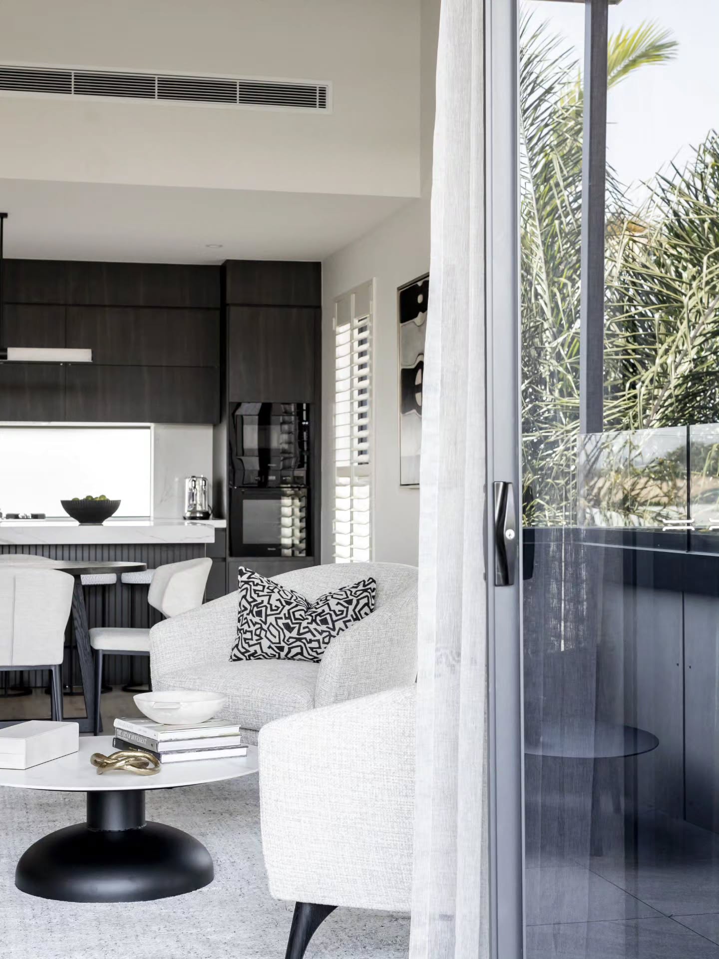 Living area looking through a sliding glass door to a palm garden, with grey armchairs — Monochrome Residence