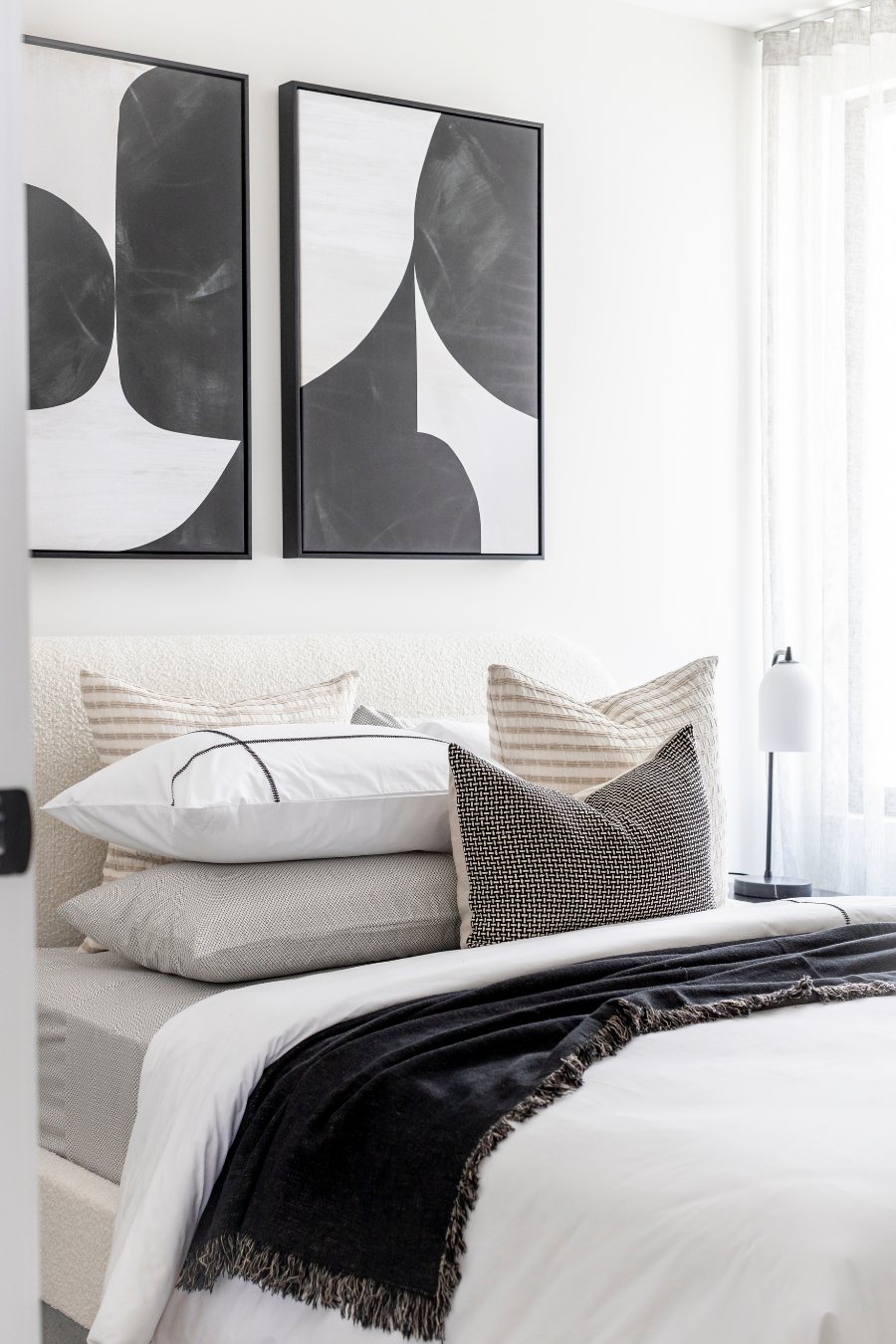 Bedhead with a pair of black-and-white abstract artworks and layered striped and textured cushions — Monochrome Residence