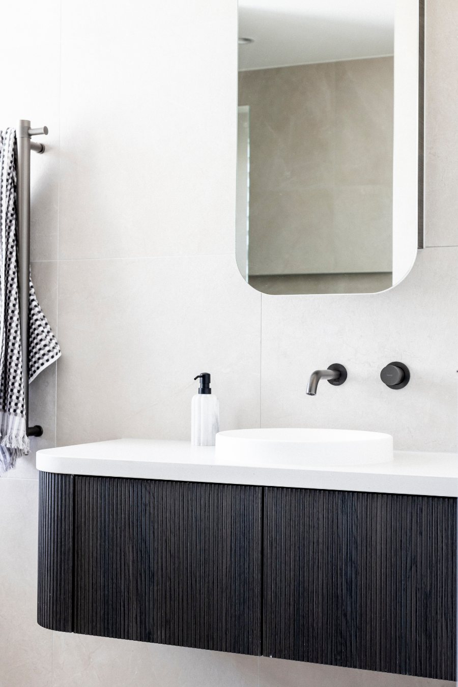 Bathroom vanity with black fluted cabinetry, a round stone basin and matte black tapware — Monochrome Residence