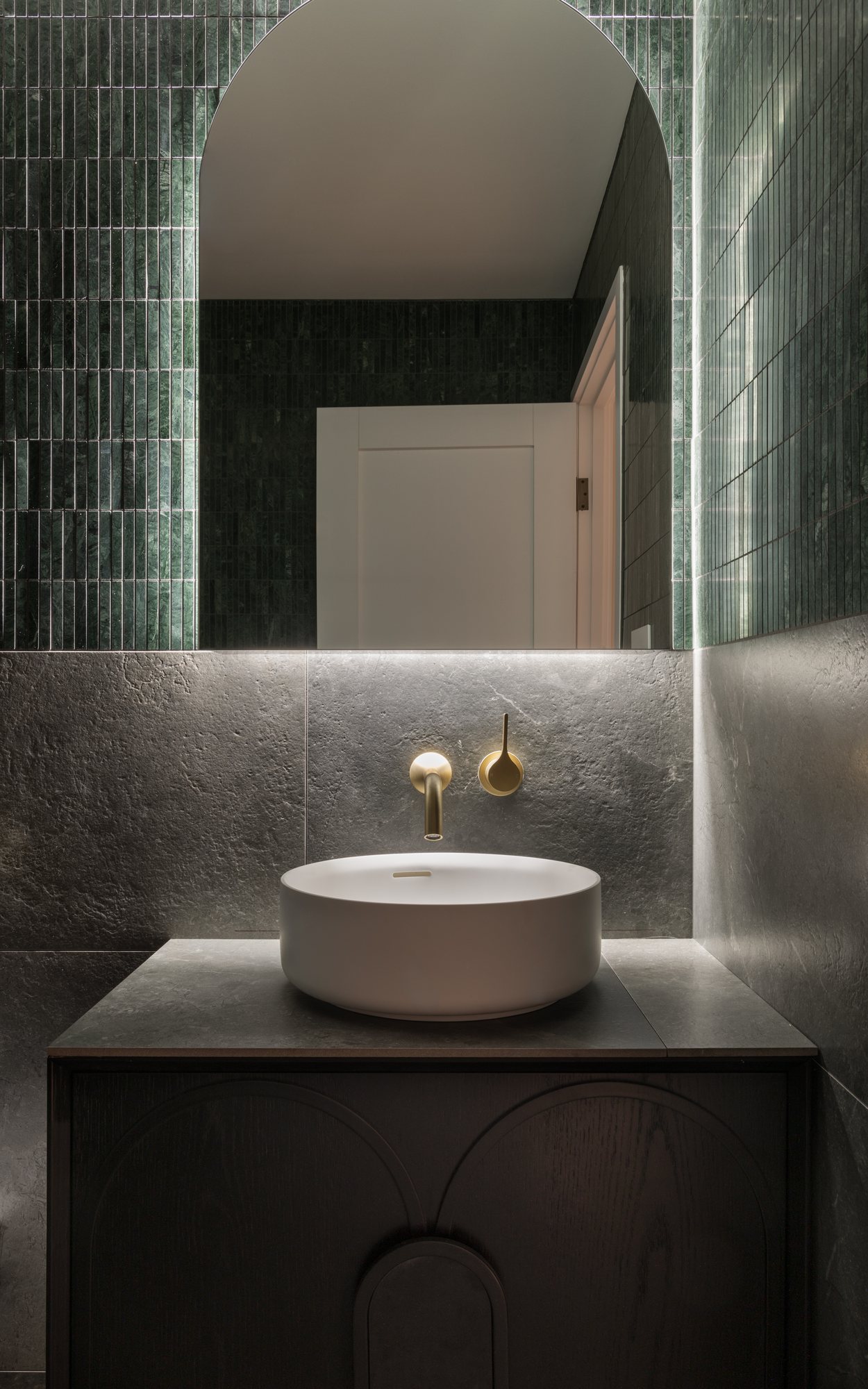 Powder room with a stone vessel basin, backlit arched mirror and brass tapware — Nundah