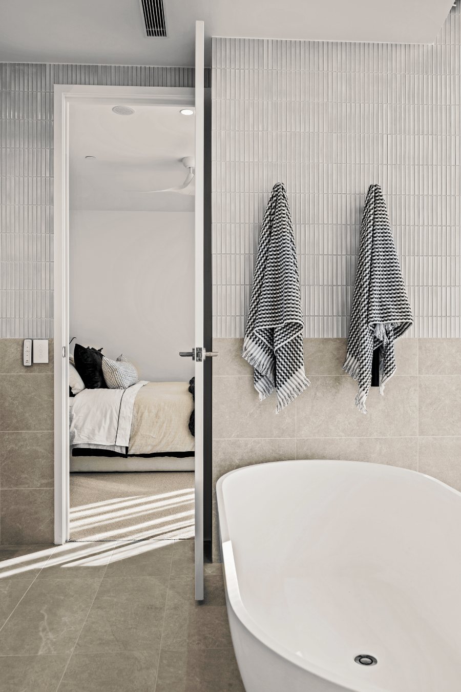 Bathroom with tiled walls, hanging towels and a freestanding tub, bedroom visible through the open door — Oceanside