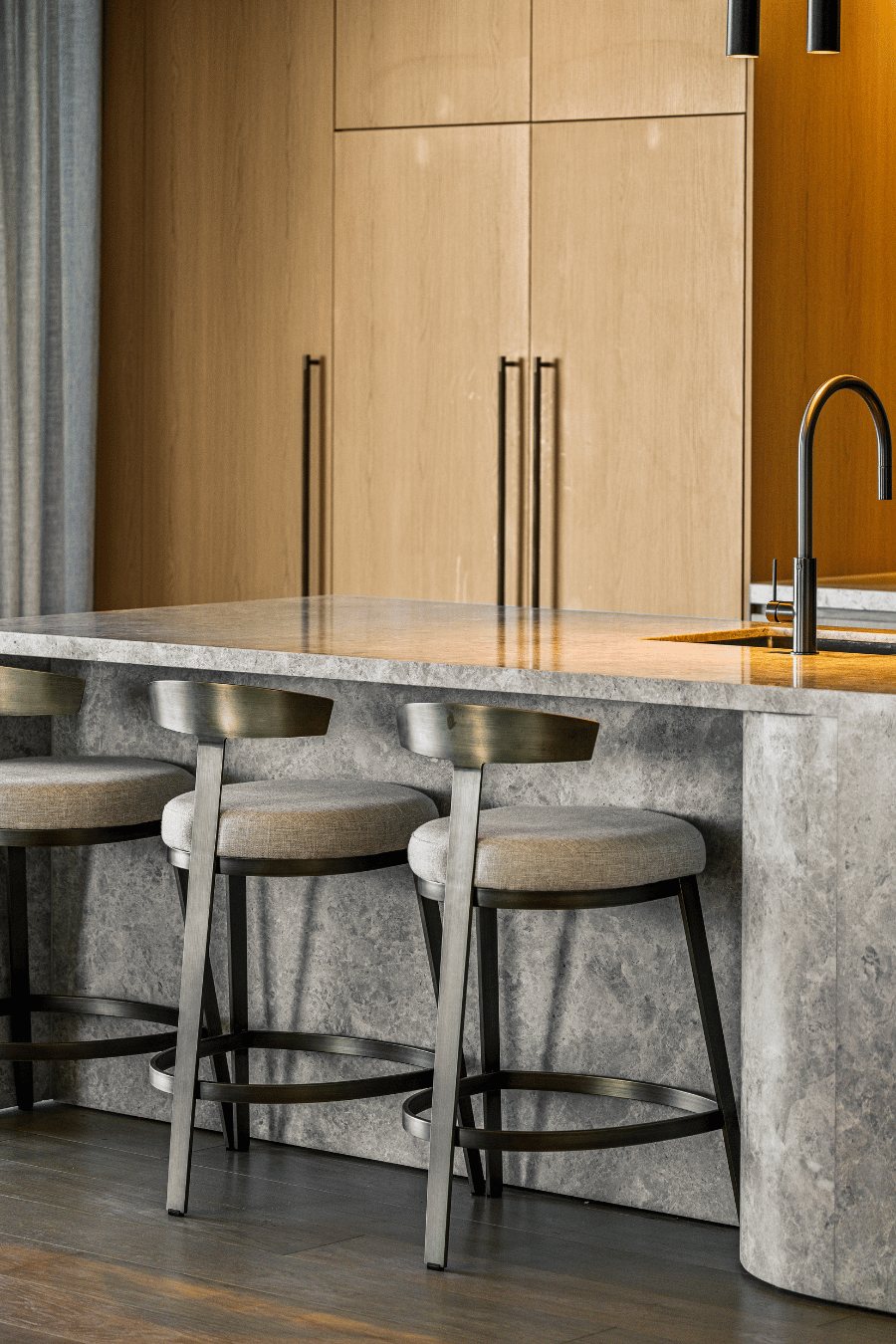 Kitchen island detail with marble waterfall benchtop, bar stools and a brass gooseneck tap — Oceanside