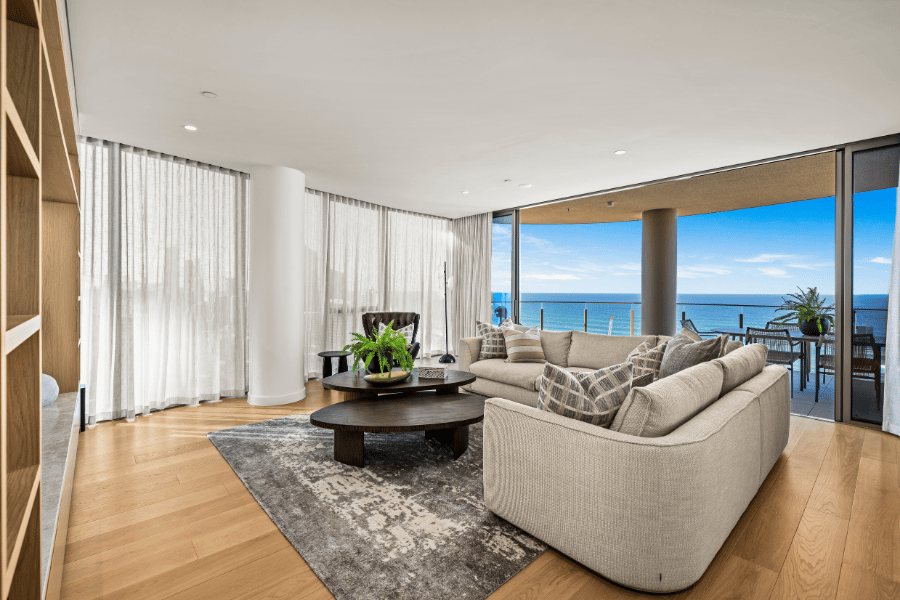 Living room with a beige sectional and dark round coffee tables facing floor-to-ceiling ocean views — Oceanside