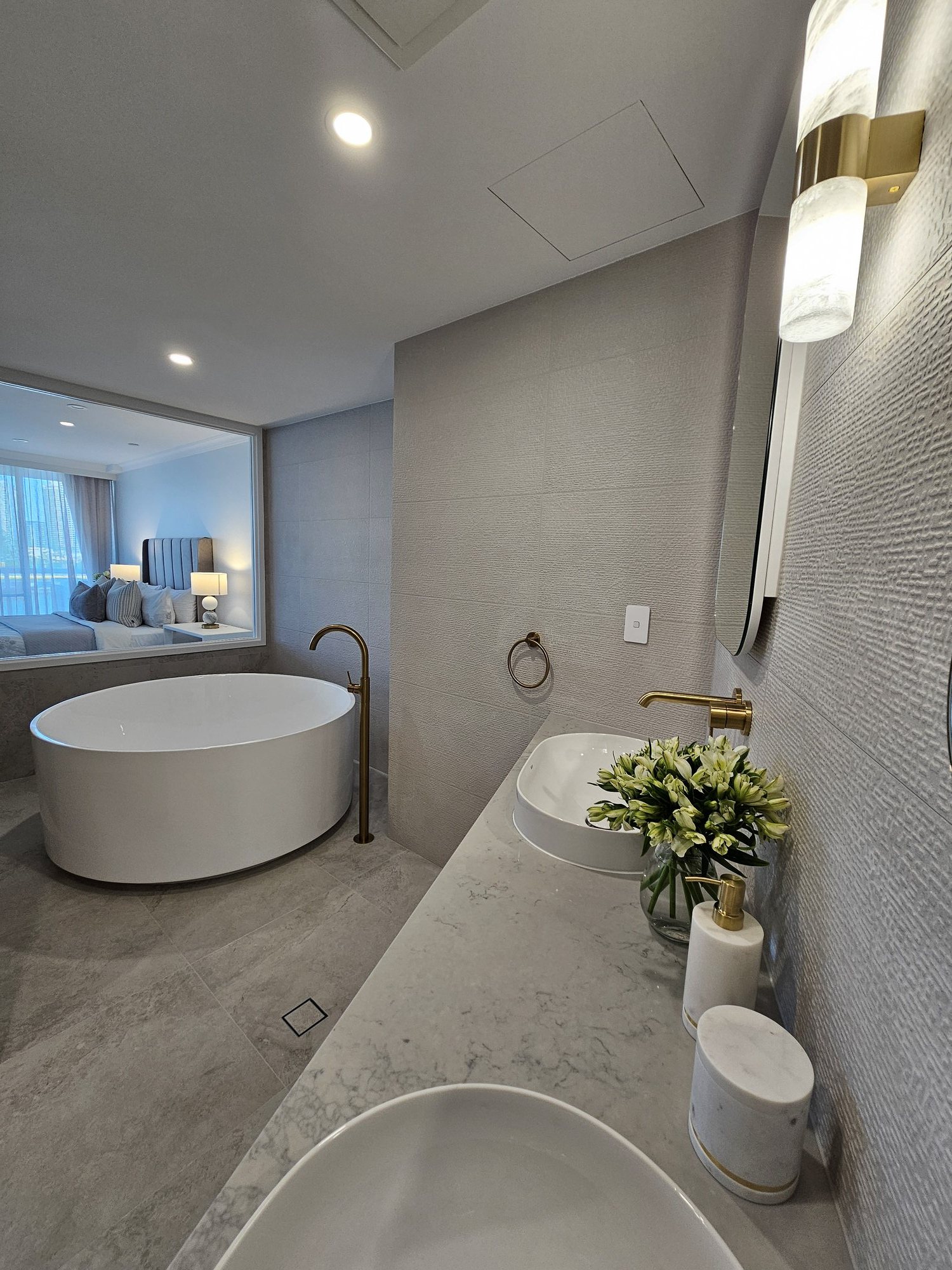 Freestanding bath with a marble vanity, brass tapware and the bedroom visible through an internal window — Rivage