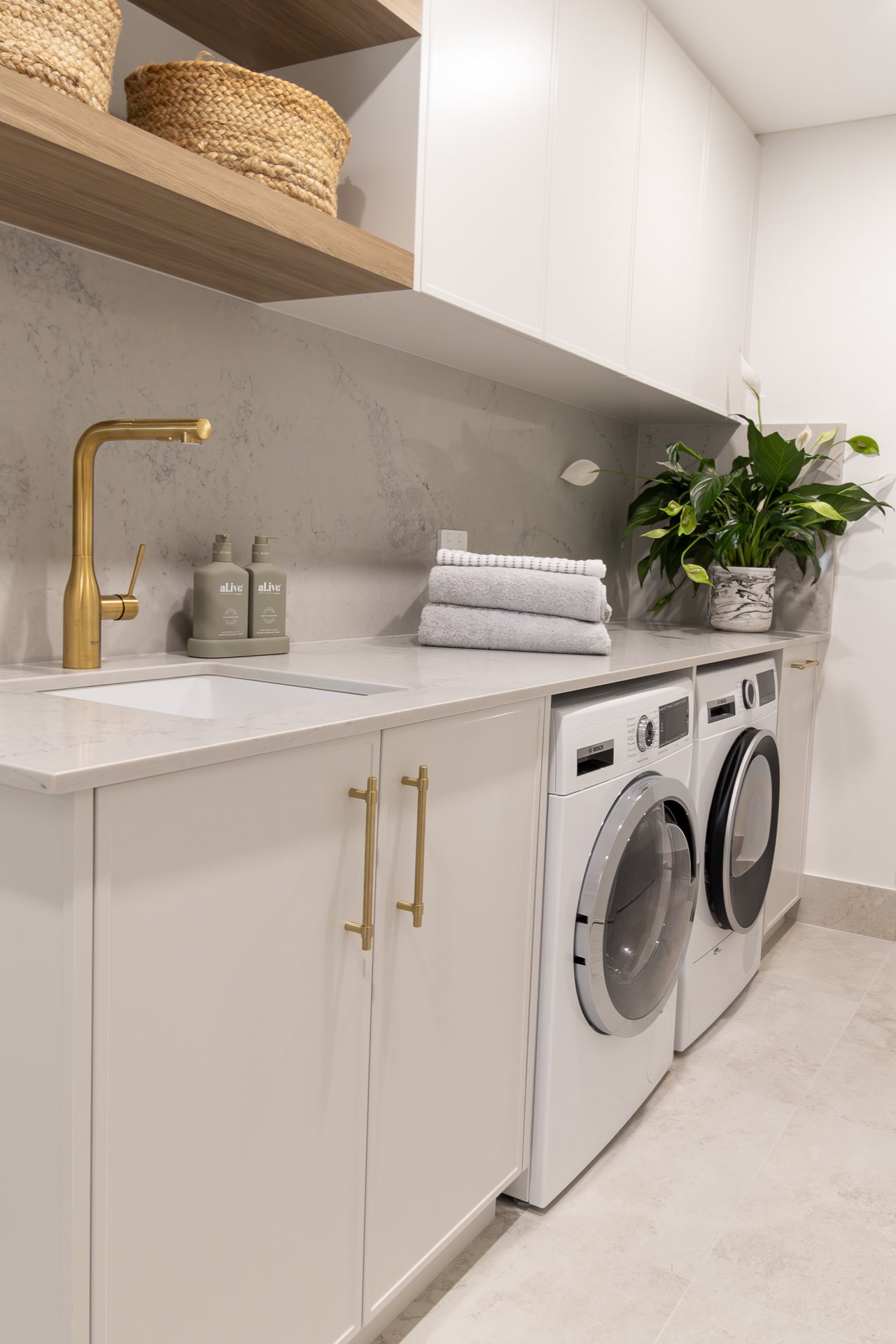 Laundry with a stone benchtop, brass tapware, open timber shelving and integrated appliances — Rivage
