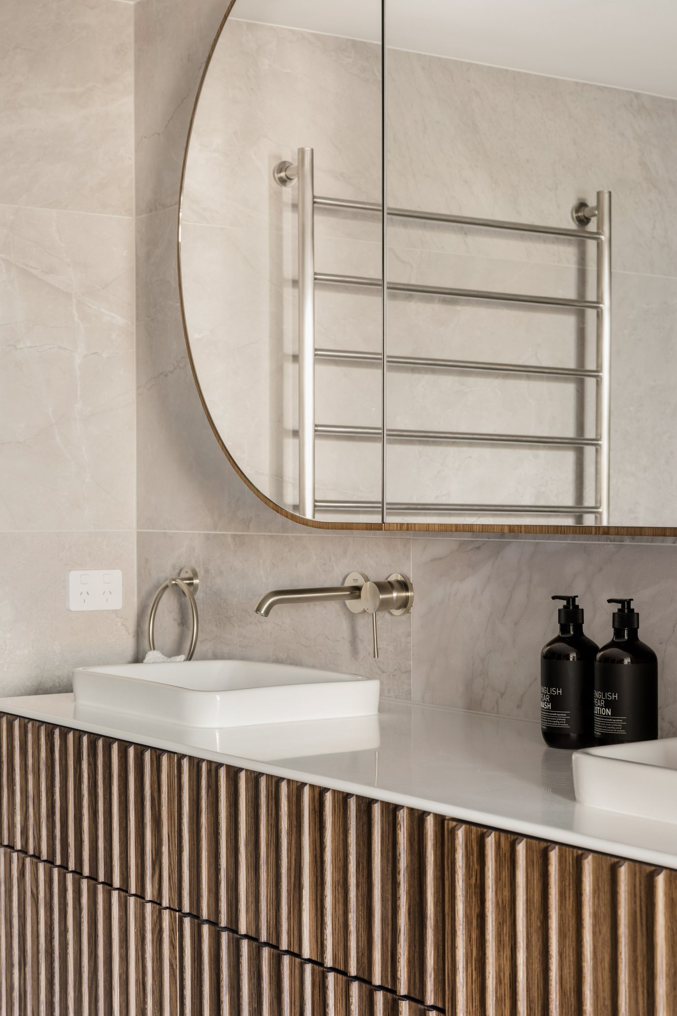 Bathroom vanity with a round mirror, heated towel ladder and fluted timber cabinetry — Stradbroke Villa 8