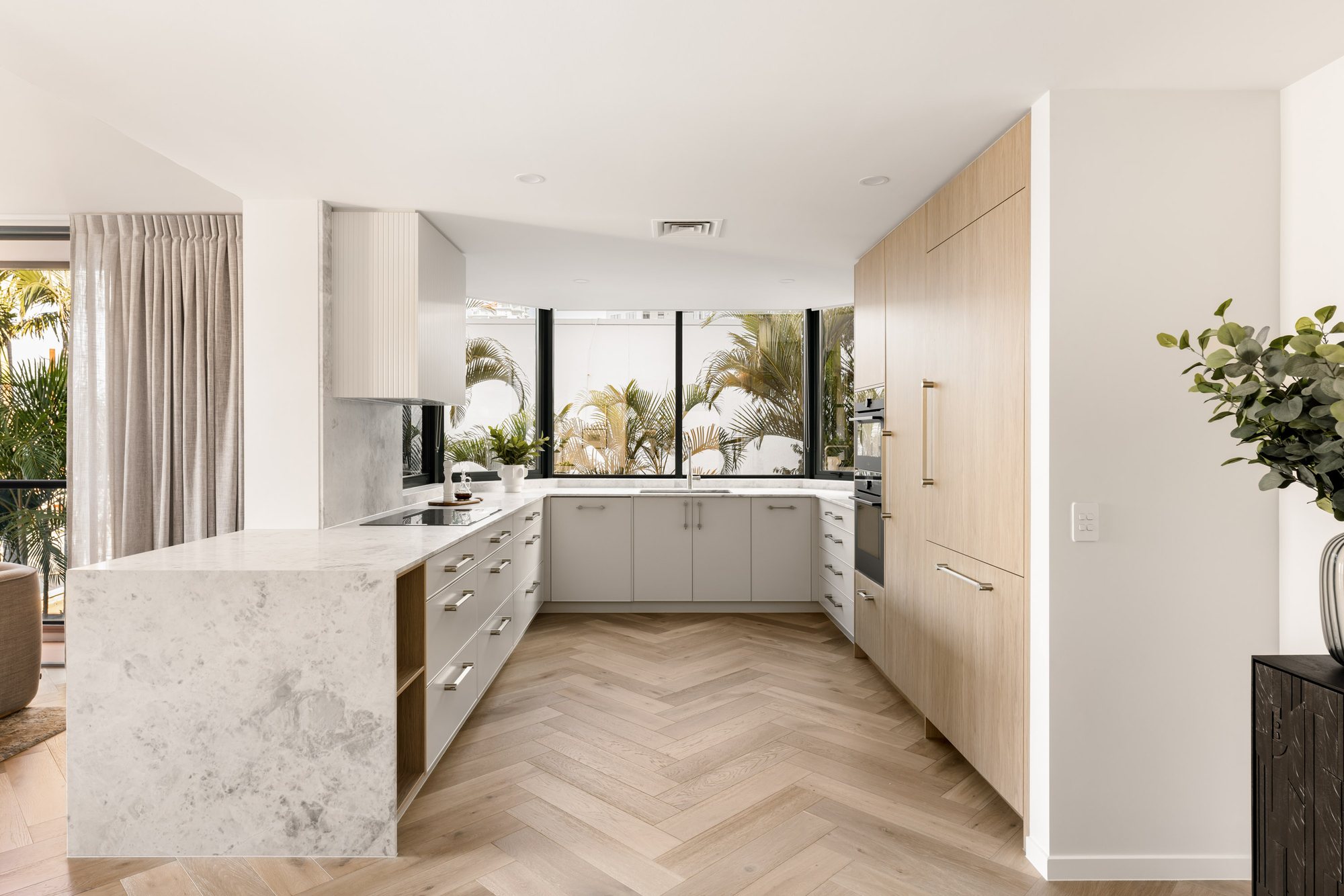 Open-plan kitchen with a marble waterfall island, white U-shaped cabinetry and herringbone flooring — Stradbroke Villa 8
