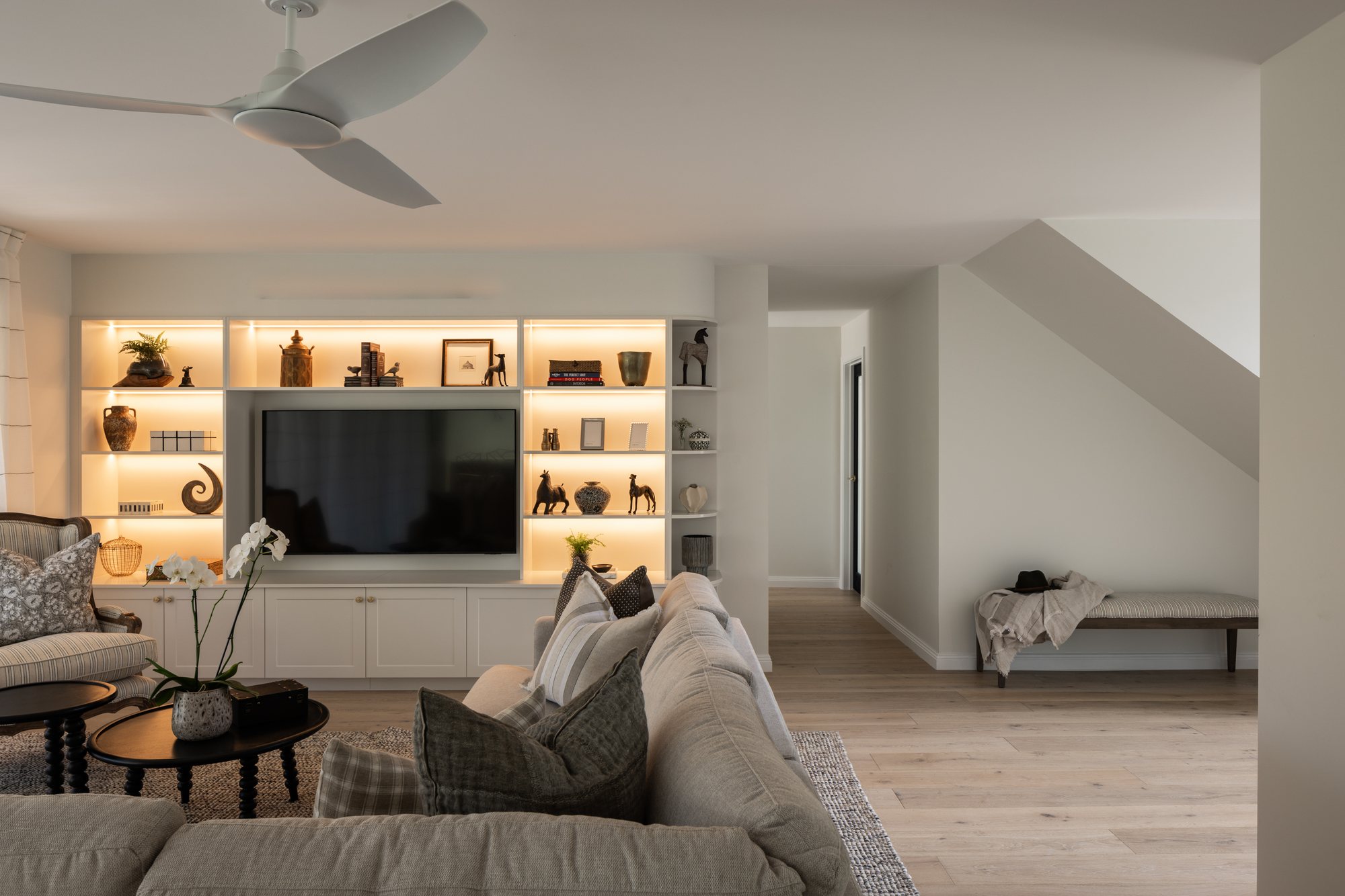 Living room with a lit built-in shelving unit around the TV and a striped armchair — The Manor House