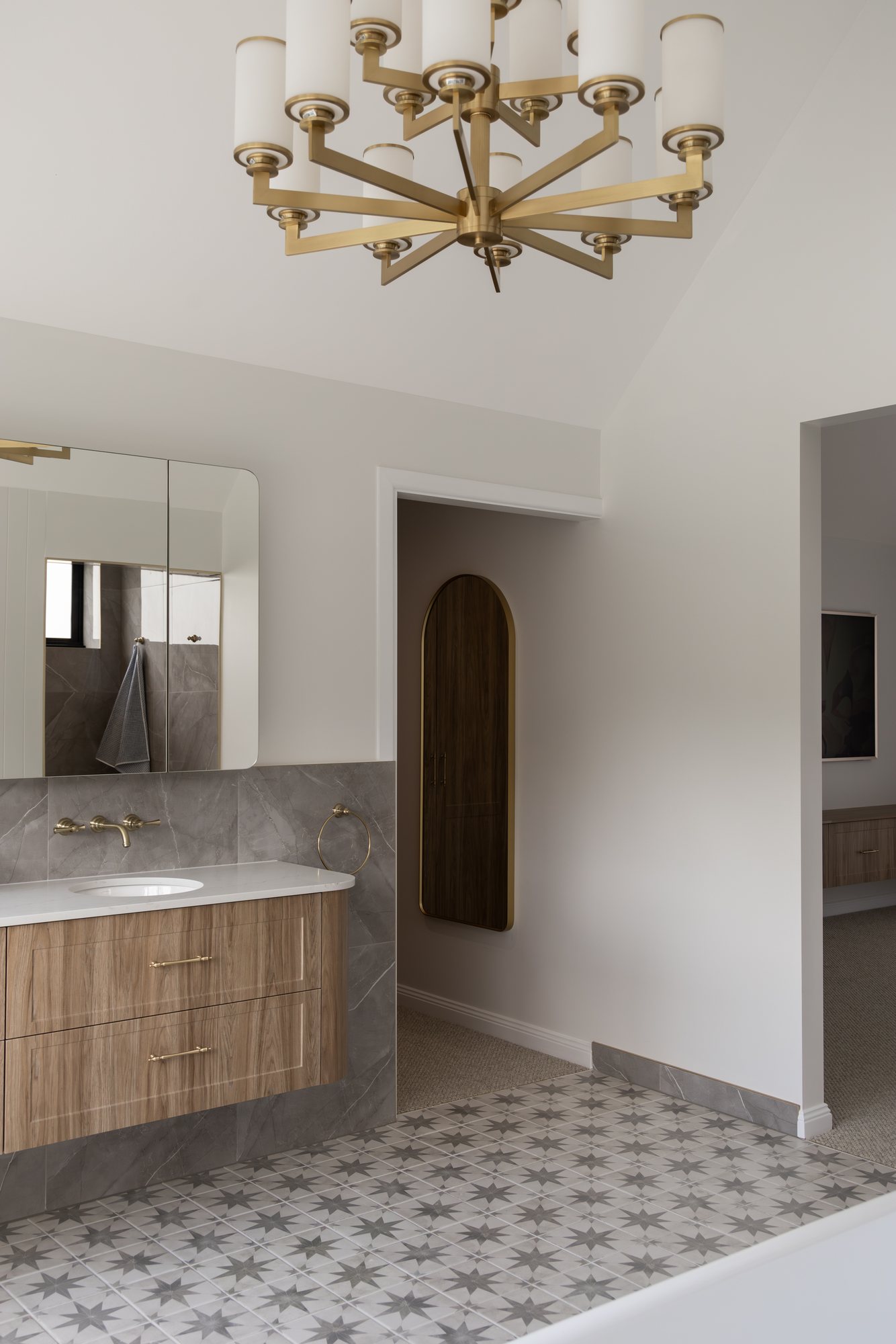 Bathroom vanity with a brass chandelier, arched storage nook and patterned floor tiles — The Manor House