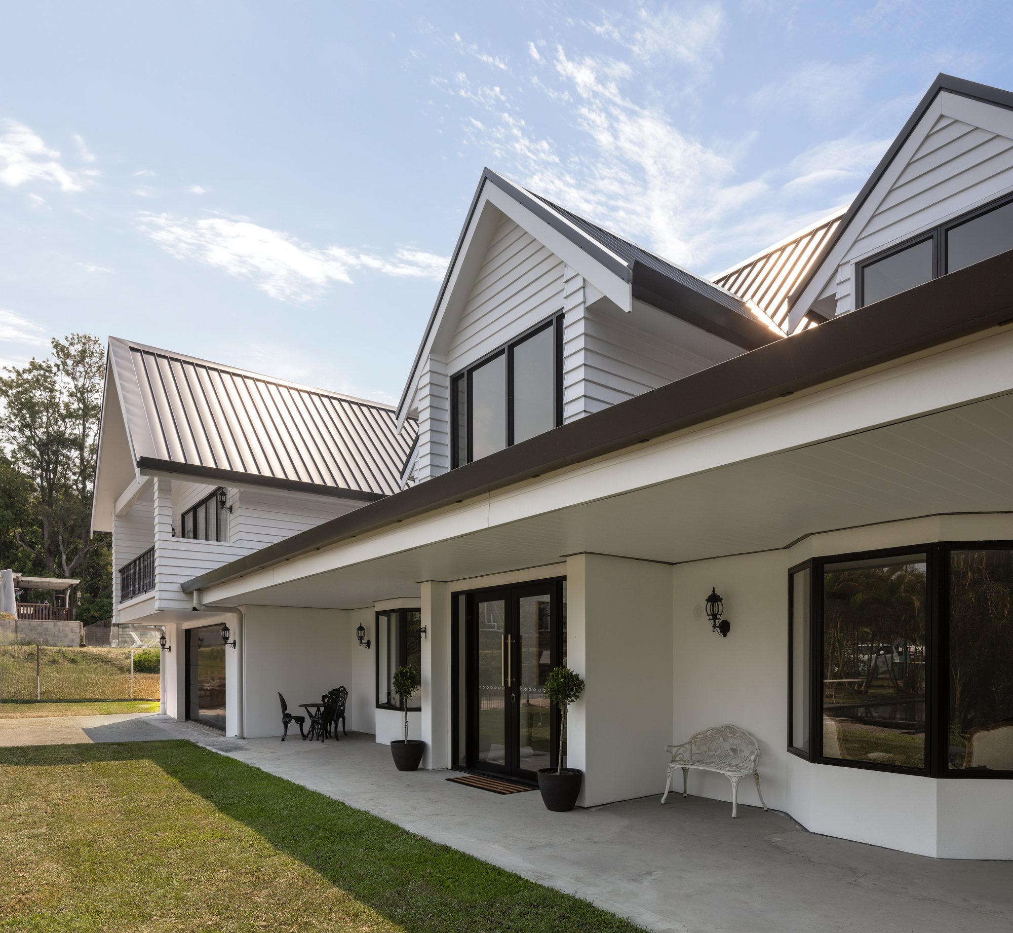 White weatherboard Hamptons-style home with a dark standing-seam roof and wraparound verandah — The Manor House